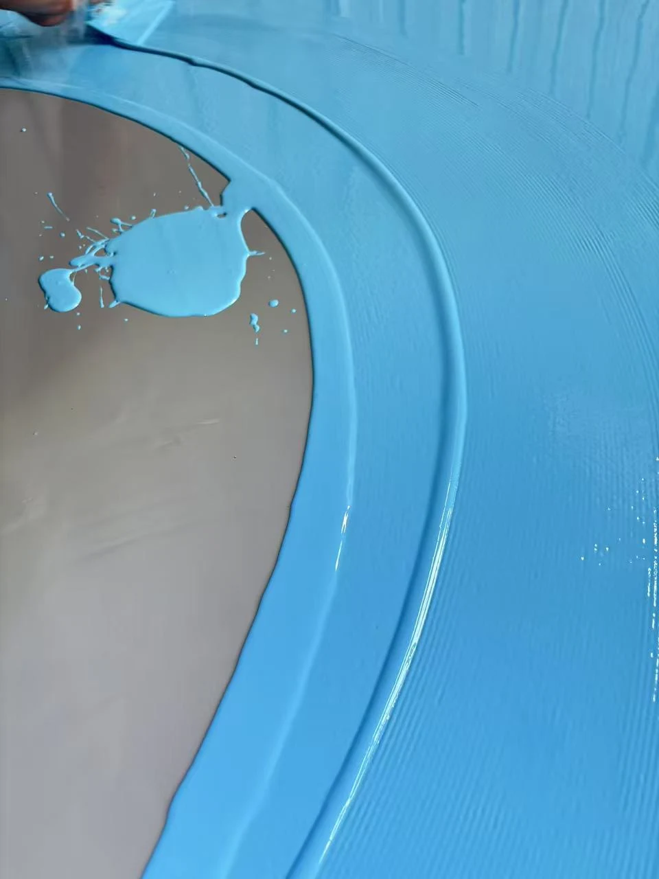 Blue coating spreads on grey substrate with scratching texture on the edge.